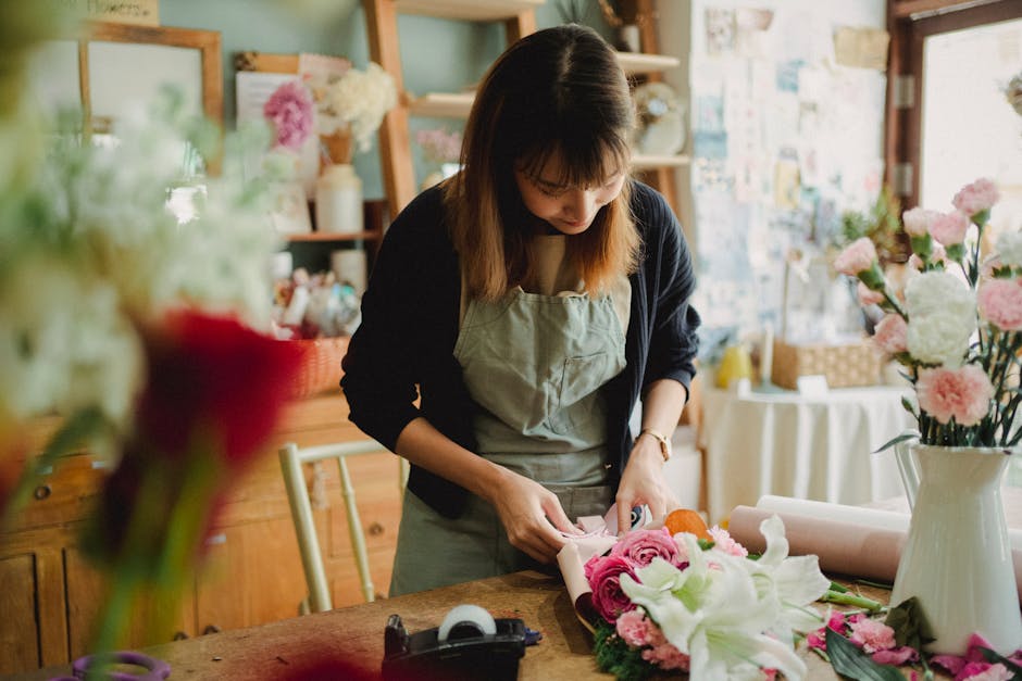 Concentrated Asian female florist arranging flowers in bouquet while working in floral shop