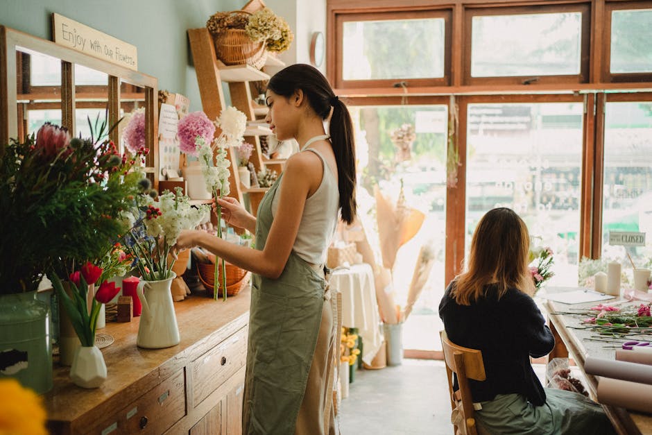 Concentrated women in casual clothes and aprons making bouquets of fresh flowers while working in cozy floristry studio
